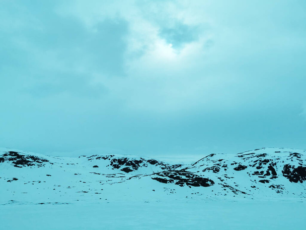 A snowy mountain in Viken, Norway, in front of a field on spring - 写真・画像