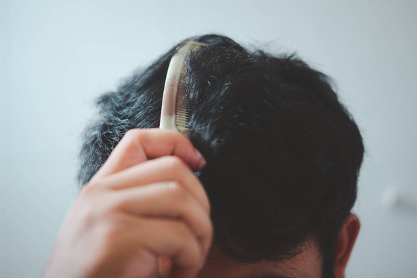 Close up young man combing his hair with a plastic comb. Styling hair. - Photo, Image