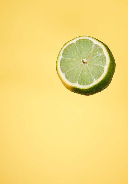 A closeup shot of a slice of lime with extract oil against a yellow background - Fotografie, Obrázek