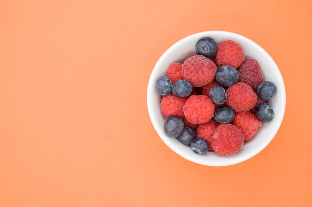 A top view of fresh blueberry and raspberry on a white bowl - Zdjęcie, obraz