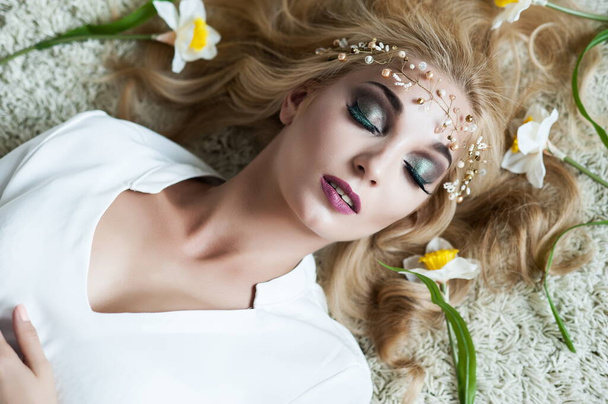Portrait of a beautiful sexy blonde girl with a headdress lying with flowers in her hair - Foto, afbeelding
