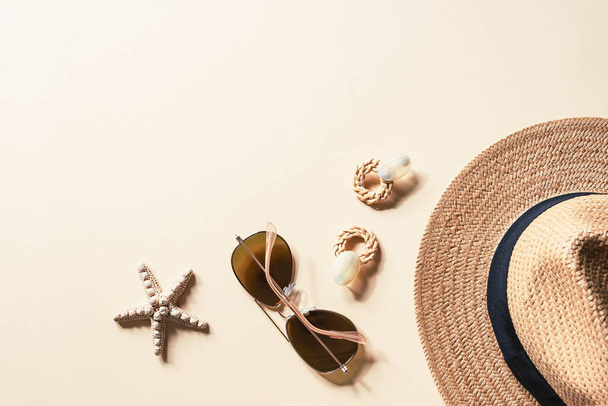 Vlakke lay met vrouwen zomer accessoires op neutrale achtergrond. Zonnebril, strohoed, oorbellen en zeesterren. Zomer reisconcept. Bovenaanzicht, kopieer ruimte - Foto, afbeelding
