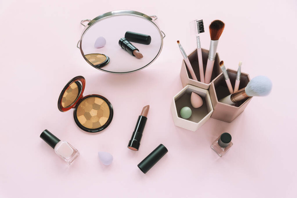 Rouge, Kosmetikpinsel, Lippenstift, Nagellack und Spiegel auf rosa Hintergrund. Schönheit, Modekonzept. Ansicht von oben - Foto, Bild