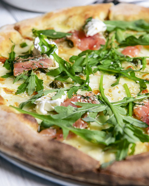 Pizza with mozzarella, salmon slices, fresh arugula. Isolated on white background. Italian cuisine concept, traditional pizza recipe. - Фото, зображення