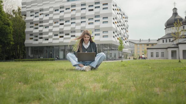 Rušné atraktivní dívka pracující na notebooku jako sedí na trávě v městském parku za hektického letního rána, venkovní záběr v městské oblasti. Student studující na počítači, který sedí na schodišti před školou. - Fotografie, Obrázek