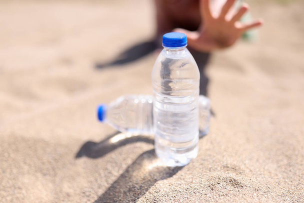 Mann greift nach Wasserflasche, die auf Sand steht - Foto, Bild