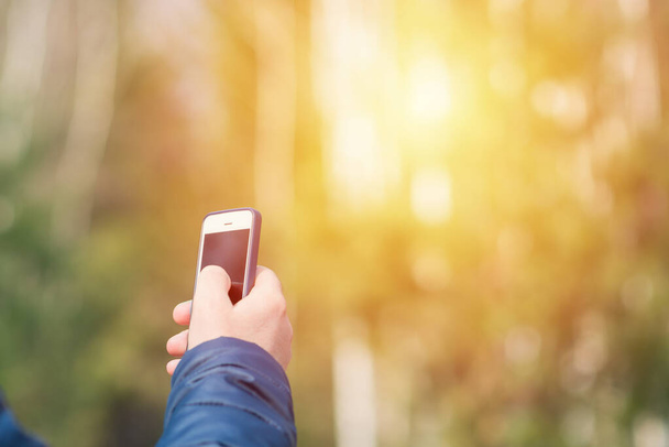 Un hombre con su teléfono inteligente móvil en busca de señal de recepción en el bosque soleado de primavera. - Foto, Imagen