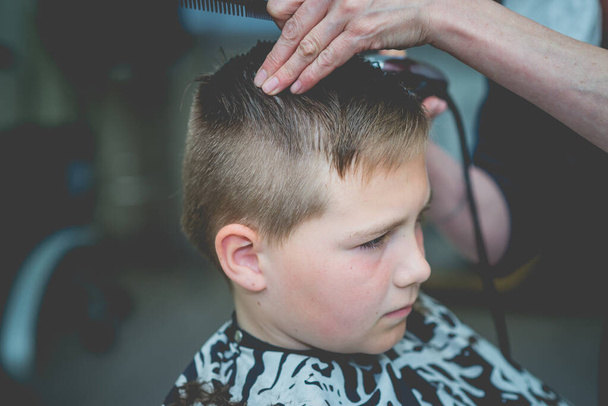 Милий хлопчик має стрижку для волосся, професійний перукар робить зачіску. Перукарня для дітей. Дитячі портрети збоку в перукарні. Телефонували
. - Фото, зображення