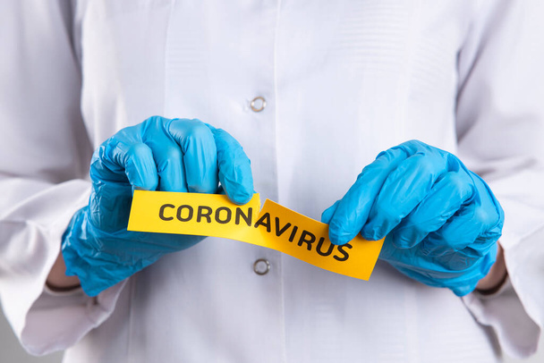 A koronavírus karantén koncepciójának vége. Fiatal, egyenruhás női orvos széttépi az újságot a Coronavirus szóval. A COVID-19 járványnak vége. - Fotó, kép
