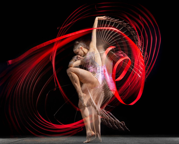 Mladá půvabná dívka rytmické gymnastka v pohybu izolované ve smíšeném světle na tmavém pozadí. - Fotografie, Obrázek