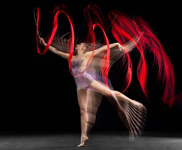Młoda piękna dziewczyna gimnastyczka rytmiczna w ruchu odizolowana w mieszanym świetle na ciemnym tle. Stroboskop - Zdjęcie, obraz