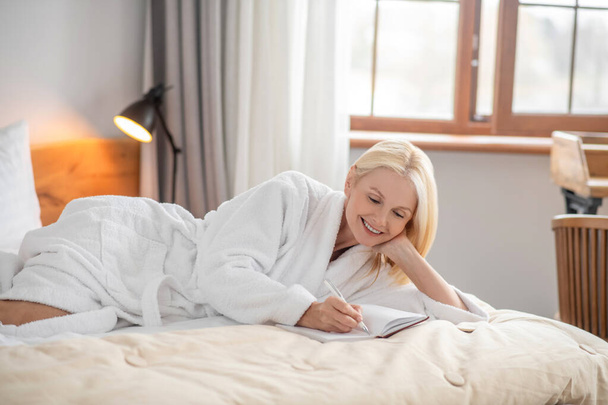 A cute woman lying on the bed and making notes - Фото, изображение