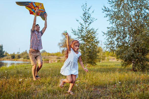 父の日だ。夏の公園でカイトと遊ぶことを楽しんでいる父と娘。家族の時間だ。男と子供が走り - 写真・画像