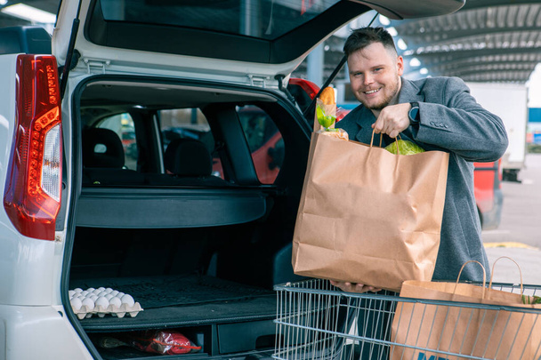 man putting bags with product in car trunk copy space - Foto, imagen