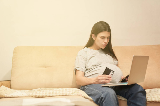 Mujer embarazada en casa con teléfono está sentado con el ordenador, compras en línea - Foto, imagen
