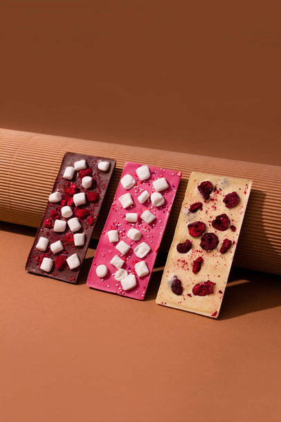 Vertikální obraz s přírodní organickou čokoládovou tyčinkou se sublimovanými bobulemi a ovocem, malinami a třešněmi, na hnědém papíře na pozadí s kopírovacím prostorem. Trendy image pro čokoládovou značku bez cukru - Fotografie, Obrázek