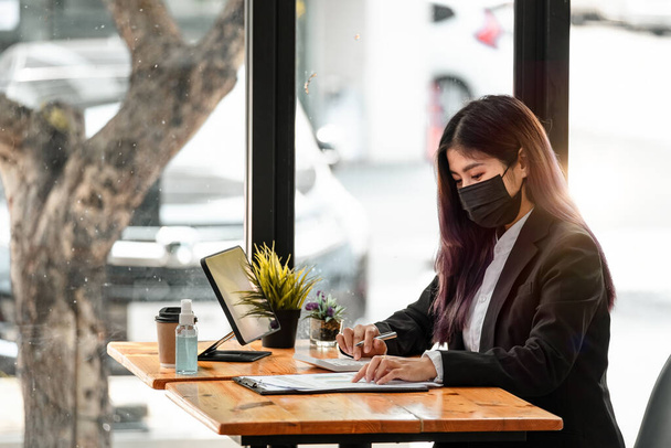 Ofisteki bilgisayarda çalışırken Asyalı iş kadınının yüz maskesi takması. Hijyen ve güvenlik kavramı. - Fotoğraf, Görsel