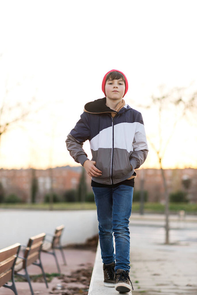 Elegante chico adolescente guapo con chaqueta de mezclilla y sombrero de punto sobre fondo de la ciudad de cerca - Foto, imagen