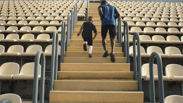 Анонимный мужчина и мальчик бегут по ступенькам стадиона - Фото, изображение
