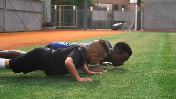 Diverso entrenador y chico haciendo flexiones en el campo - Foto, Imagen
