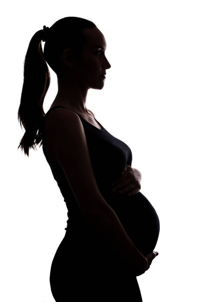 silhouette portrait of pregnant woman on white background with hands on belly, vertical - Fotografie, Obrázek