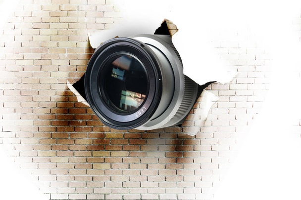 Concept of paparazzi or hidden camera, camera lens looks out through a hole in white brick wall - Photo, Image