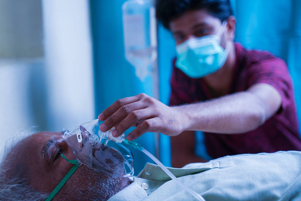 Син з медичною маскою для обличчя доглядає за хворим старим батьком у лікарні шляхом перевірки вентилятора кисневої маски концепція літніх людей охорони здоров'я та медицини
 - Фото, зображення