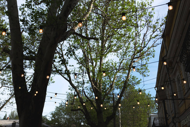 Decorated with a garland of large lamps on the summer terrace of the city cafe - Foto, Imagen