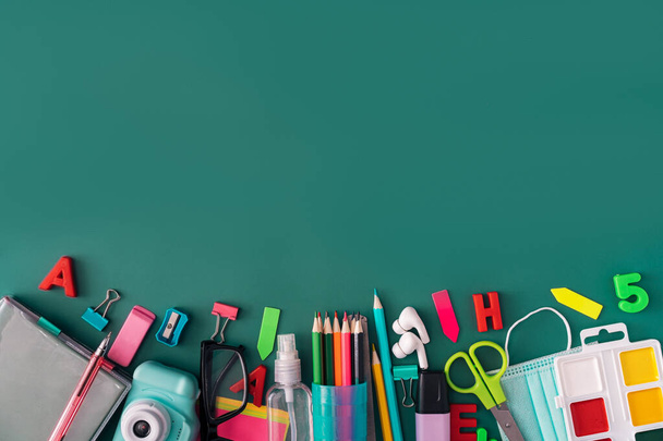 Office stationery with medical mask and headphones on green background. - Photo, Image