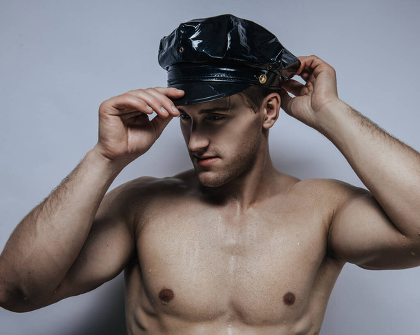 Studio portrait of shirtless young man in policeman cap - Photo, Image