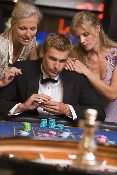 Hombre apostando en el casino rodeado de mujeres glamorosas en la mesa de ruleta
 - Foto, imagen
