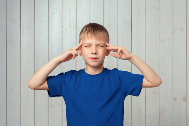 Portrait d'un garçon préadolescent confiant en t-shirt bleu pointant les doigts vers la tête, faisant un plan. Concept de pensée. Sois intelligent et réfléchis. Plan studio, fond bois clair - Photo, image