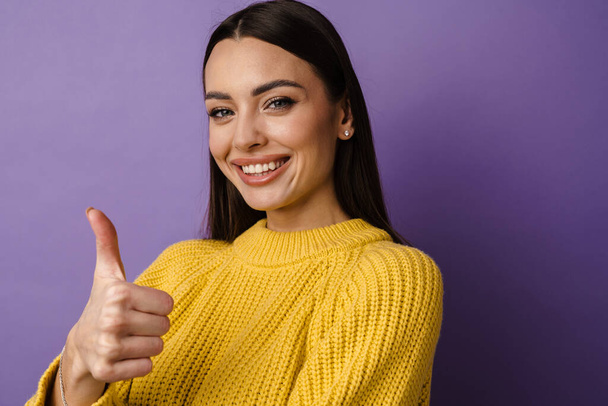 Close up of a cheerful attractive young woman in casual wear standing isolated over violet background, giving thumbs up - Фото, зображення