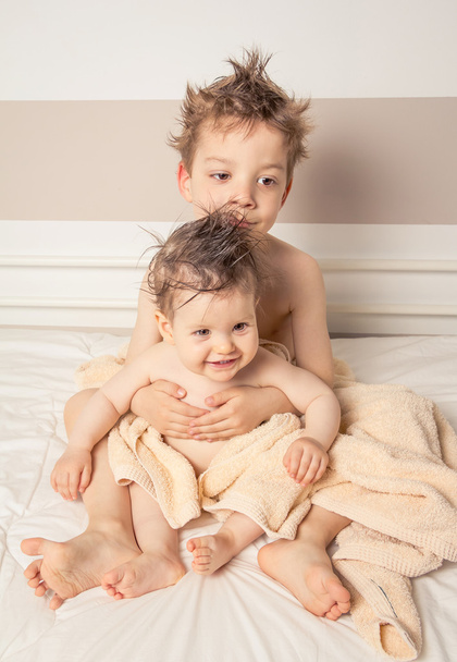 jongen en baby met natte haren onder handdoeken boven een bed - Foto, afbeelding