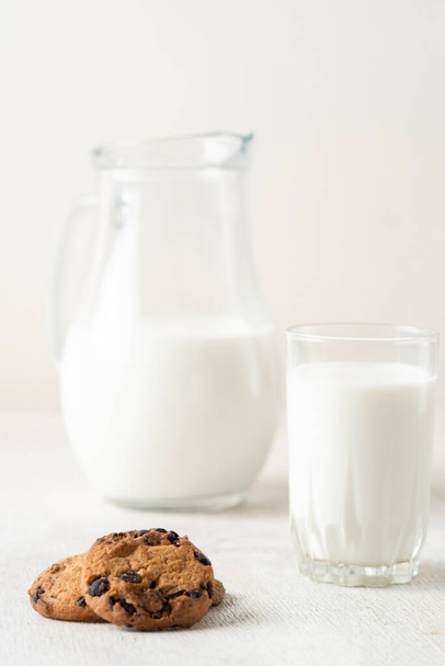 chocolate chip cookies and milk in a jug and a glass on a white wooden  background - Valokuva, kuva