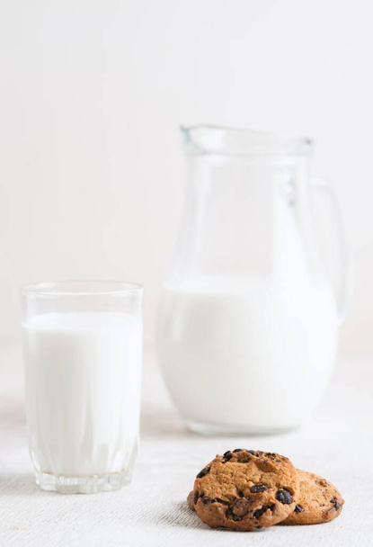 chocolate chip cookies and milk in a jug and a glass on a white wooden  background - Fotografie, Obrázek