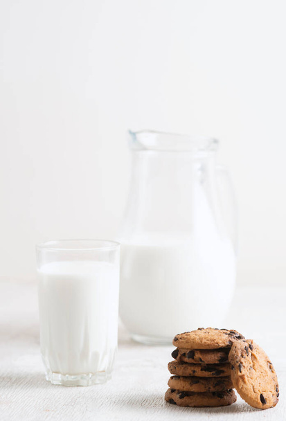 chocolate chip cookies and milk in a jug and a glass on a white wooden  background - Foto, Imagem