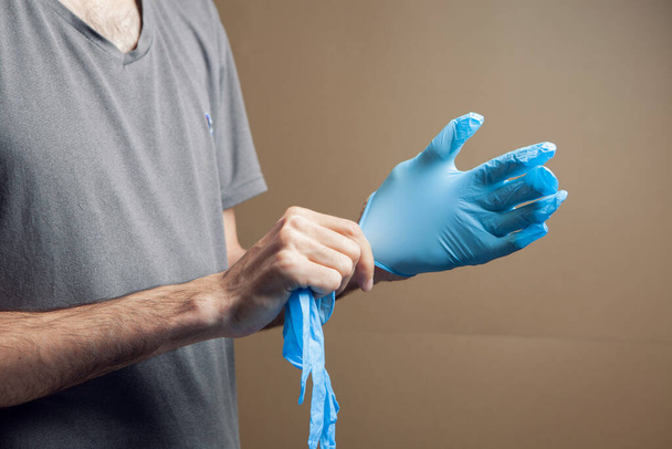 man putting on rubber gloves on brown background - Фото, изображение