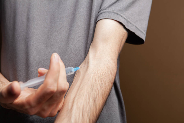 drugsverslaafde geeft zichzelf een injectie op bruine achtergrond - Foto, afbeelding
