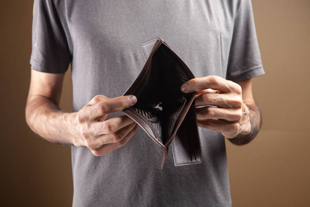 man showing empty wallet on brown background - Foto, afbeelding