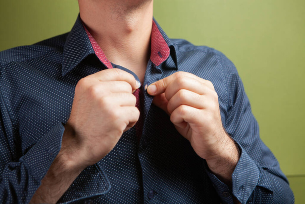 egy férfi kiegyenesíti az inge gallérjának gombját zöld alapon. - Fotó, kép