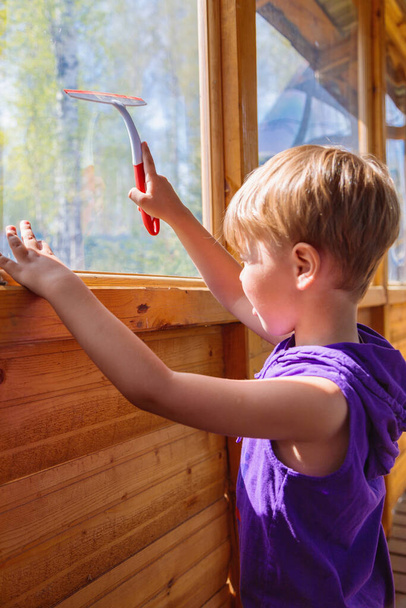 The child washes the windows with a special brush. A child with blond hair - Foto, imagen