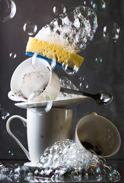 Montón de platos blancos sucios sobre fondo oscuro, con esponja de lavado y burbujas - Foto, imagen