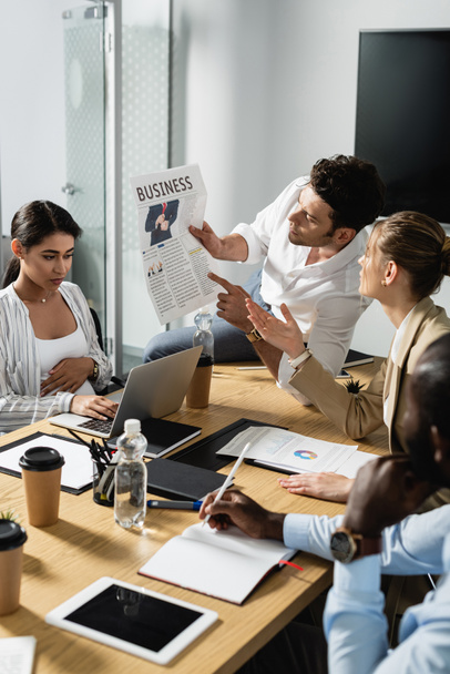 young businessman showing newspaper to multiethnic colleagues during meeting - Foto, Bild