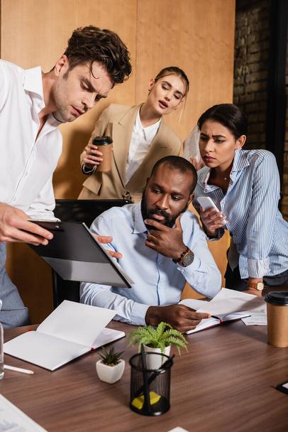 businessman showing clipboard to thoughtful multiethnic colleagues - Photo, Image