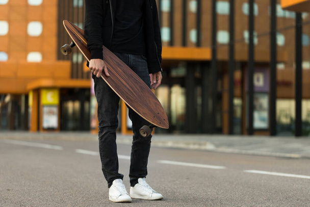 Man hipster houden skateboard of lange boord buiten, bijgesneden afbeelding. Vrije tijd, gezonde levensstijl, extreme sporten - Foto, afbeelding
