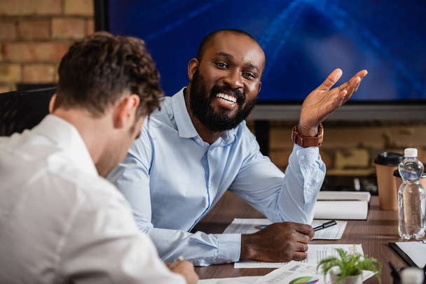 happy african american businessman looking at camera near blurred colleague - Photo, Image