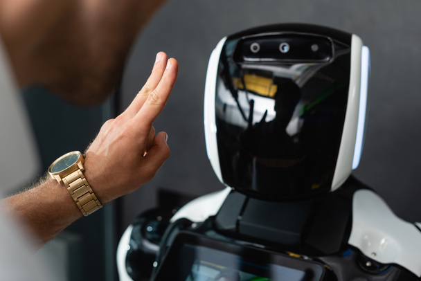 cropped view of businessman showing victory gesture near robot in office - Foto, afbeelding