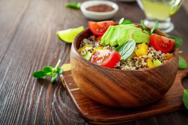 Comedor vegetariano saludable con quinua, aguacate, tomates, espinacas y semillas sobre fondo de madera. - Foto, Imagen