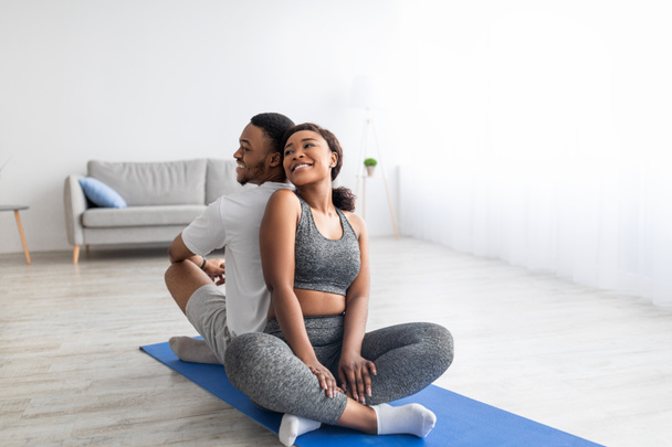 Senhora negra sentada de costas para trás com seu namorado esportivo na posição de lótus, tendo prática de ioga parceiro doméstico - Foto, Imagem